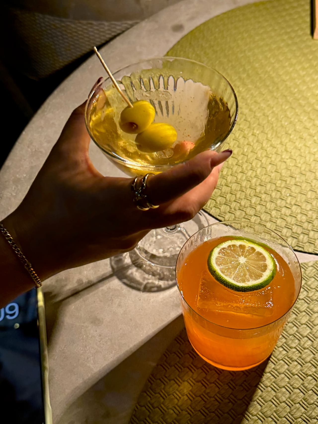 A martini and a cocktail held over a candlelit dinner table.